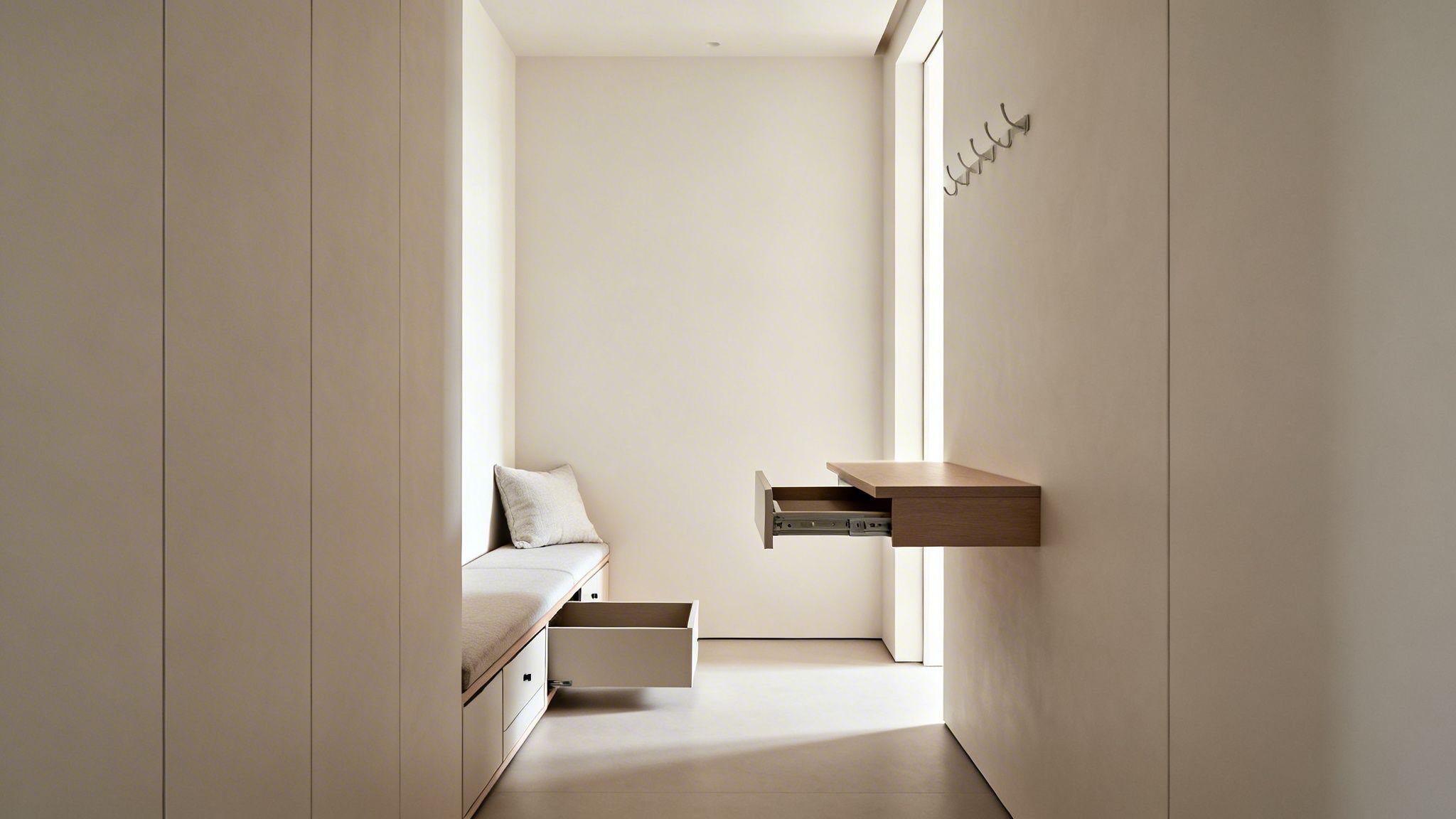 Entrada minimalista con asiento acolchado, almacenamiento en cajones y ganchos de pared.